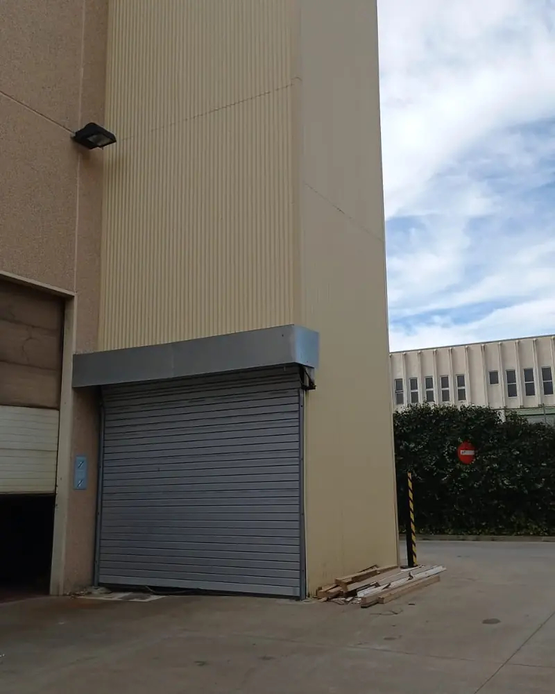 Torre exterior de un elevador con puerta enrollable a pie de calle, junto a una nave