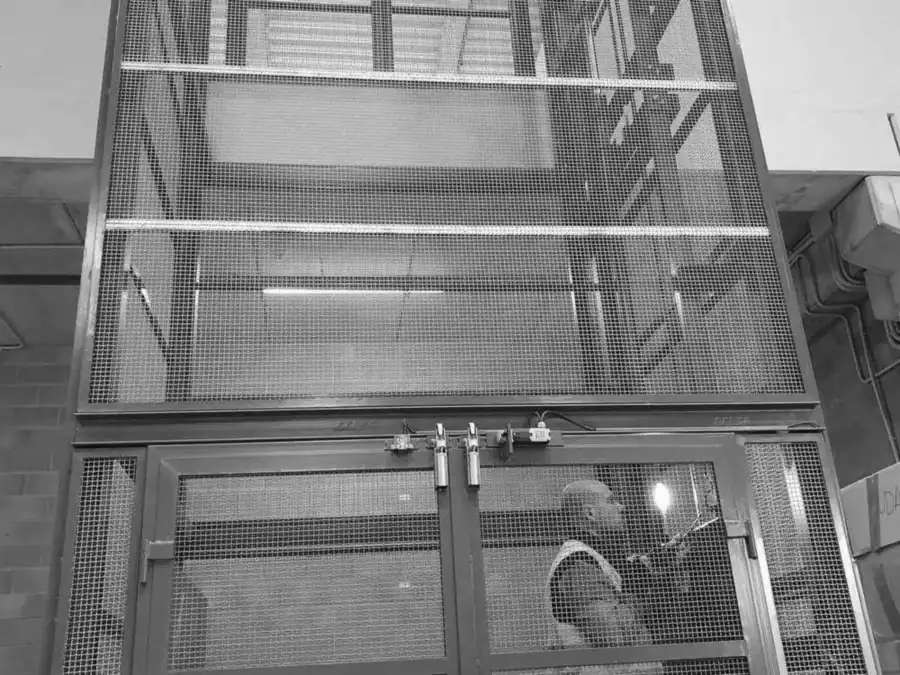 Técnico con chaleco reflectante tras las puertas de malla de un montacargas