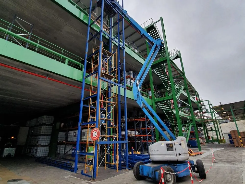 Plataforma de tijera junto a la estructura de un elevador dentro de una nave