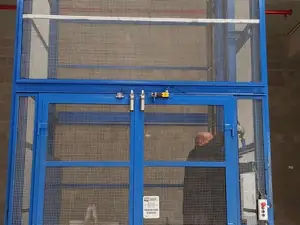 Puertas de un montacargas de malla azul con una persona en el interior de la cabina