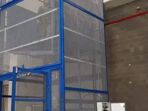 Montacargas de malla azul de gran altura junto a una pared de bloques