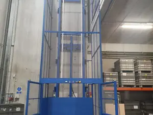 Montacargas de malla azul de gran altura en una nave, junto a cajas y estanterías
